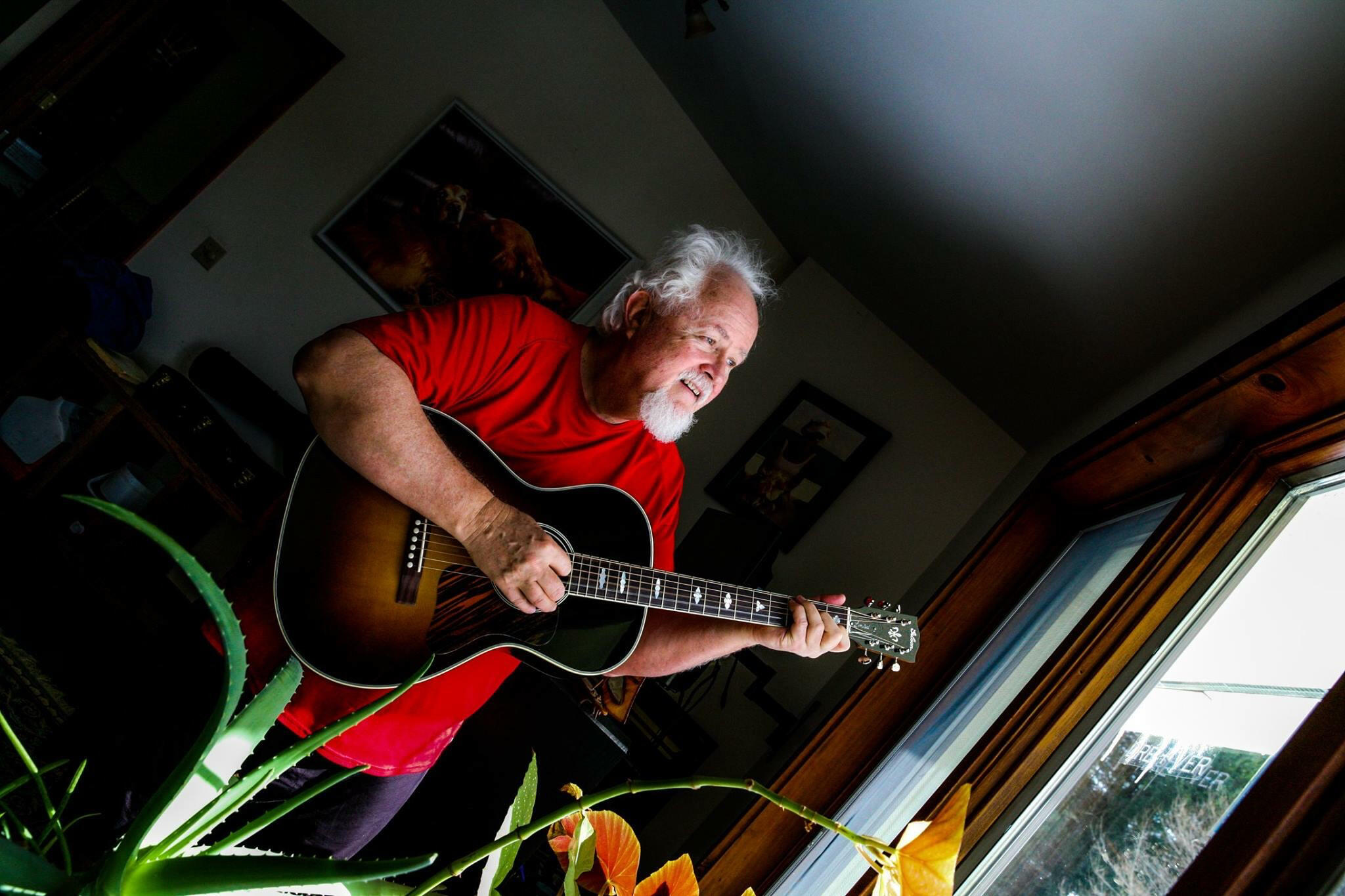 Andre J de Saint Phalle singing and playing guitar in his living room.